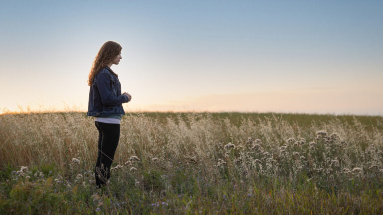 Young woman standing in a field saying her spring prayers