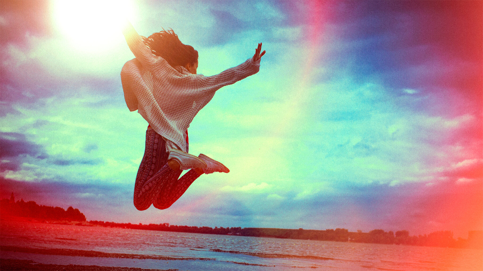 A woman on a beach leaps with joy; Getty Images