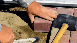 The gloved hand of a mason lines up bricks; photo credit Shutterstock