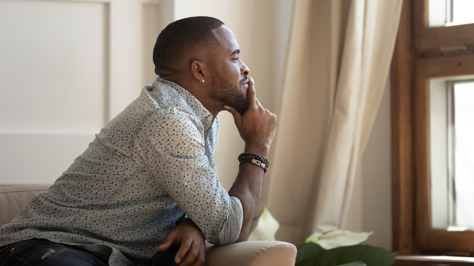 Man sits on couch in living room alone; photo by fizkes / iStock / Getty Images Plus