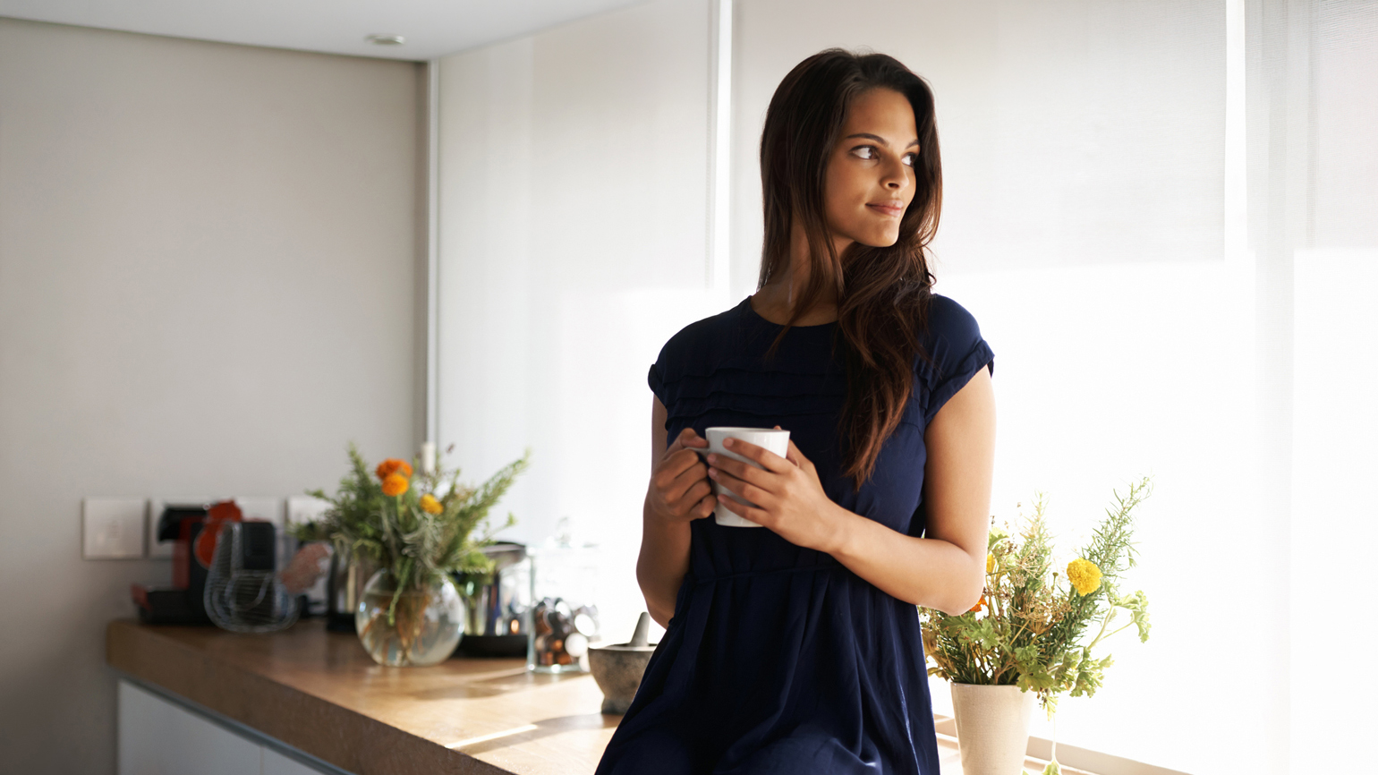 Cropped shot of an attractive young woman standing in her kitchen while drinking coffee