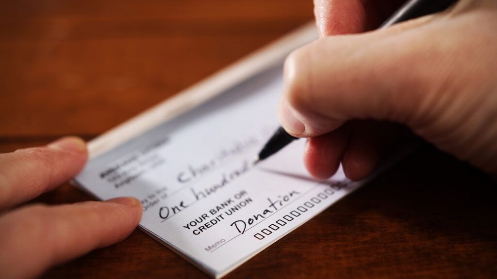 A hand writes a check for charity