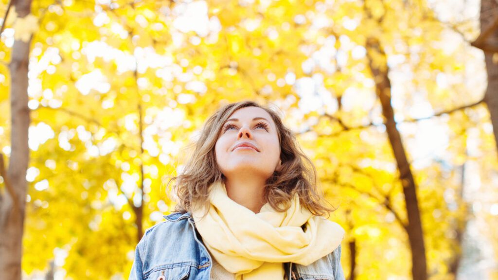 Woman looking up in autumnal park hearing inspirational thanksgiving stories