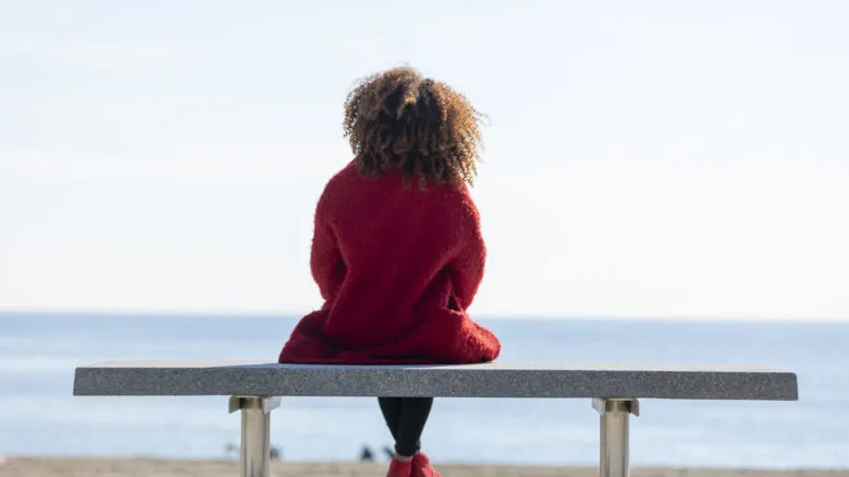 View from behind of a woman on a bench reading Valentine's Day devotionals at the beach