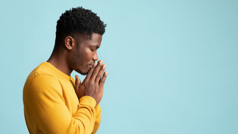 Man in a yellow sweater with blue background making a prayer habit