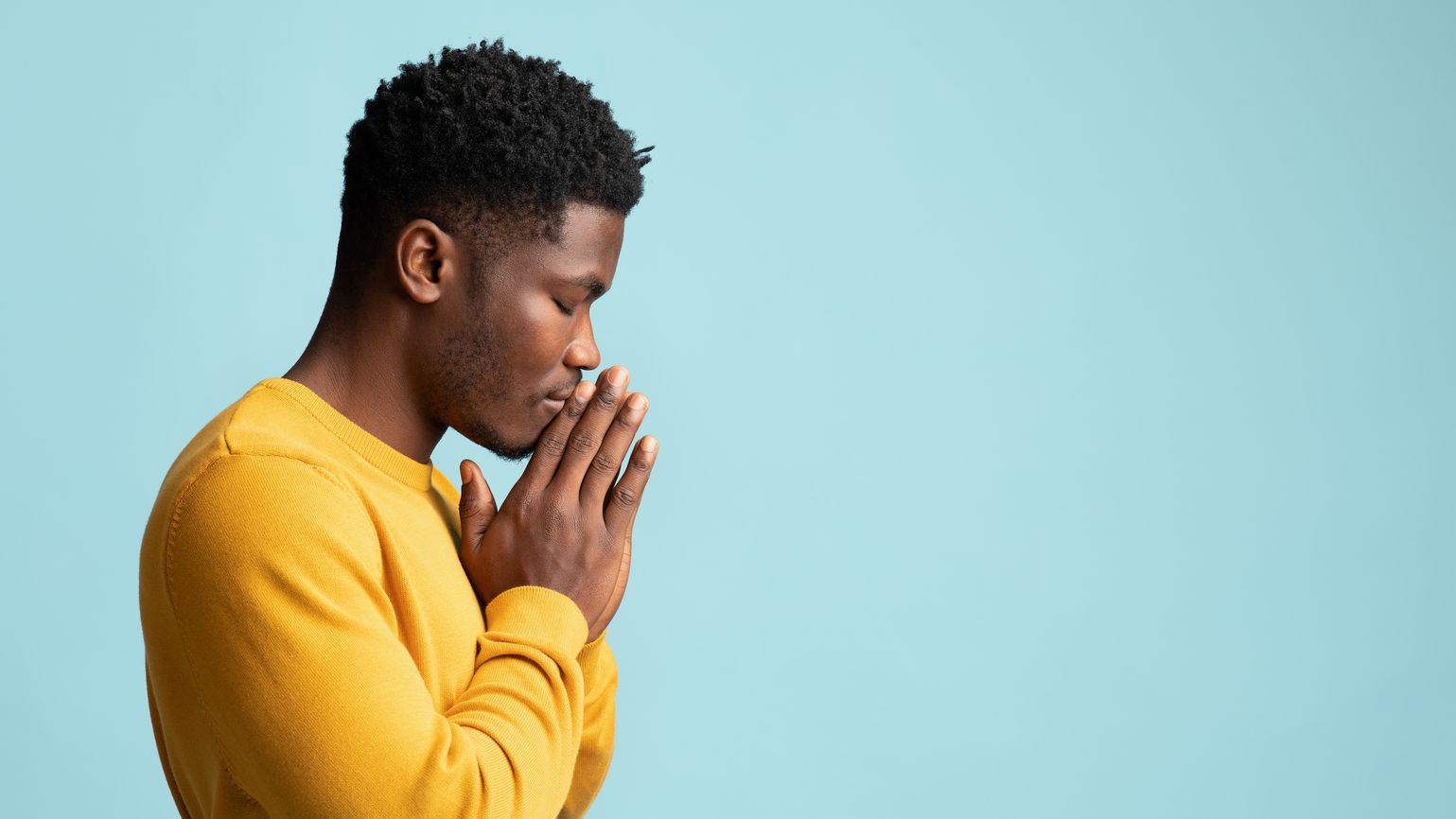 Man in a yellow sweater with blue background making a prayer habit