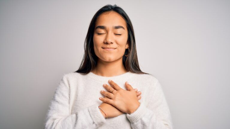 Woman in a white sweater with her hand on her heart saying her prayer habit
