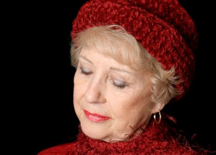 An older woman wearing a red hat who is in prayer
