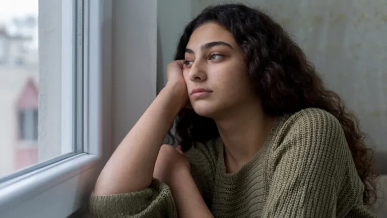 Woman sitting isolated by the window thinking of what to give up for lent