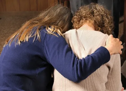 two women, one with arm around the other, heads bowed