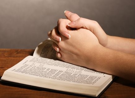 praying hands resting on a Bible