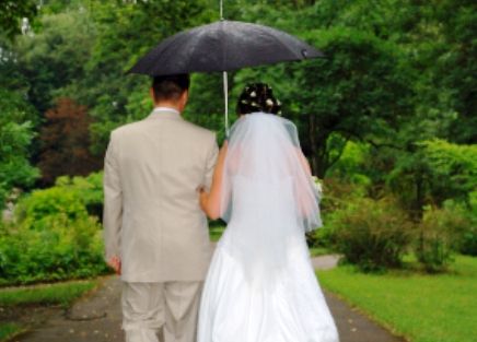 Wedding couple in the rain beneath an umbrella.