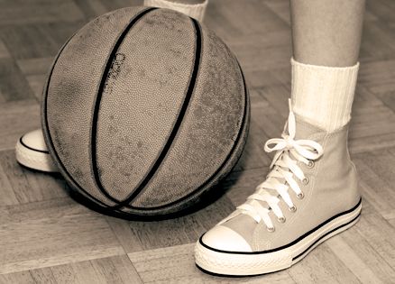 A sepia photo of a weathered basketball and a pair of feet in high-tops