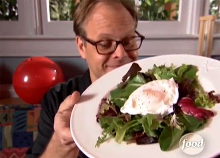 Alton Brown poses with a poached egg atop a green salad