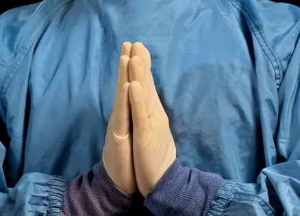 A doctor's gloved hands clasped in prayer