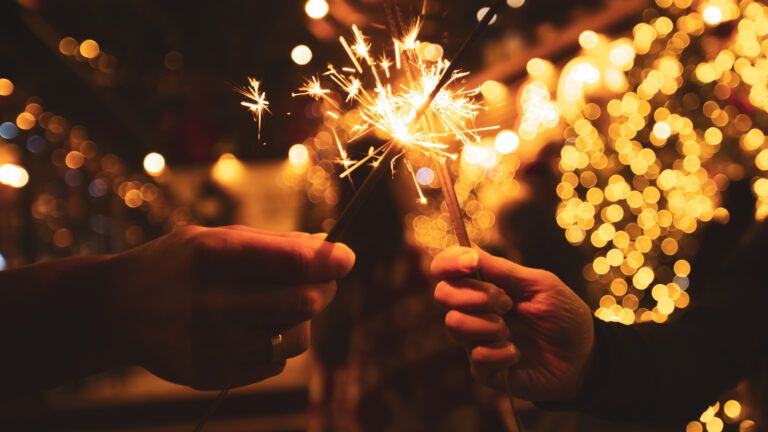 Two hands holding sparklers with lights in the background after reading a new year devotional