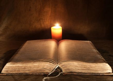 An old holy book illuminated by a small candle