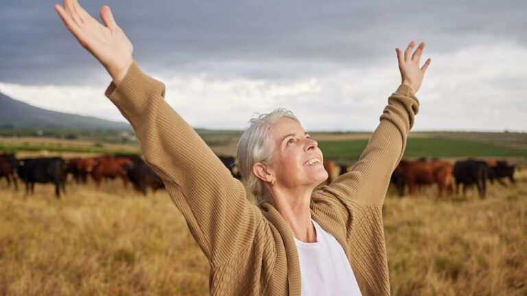 Senior woman in a field with cows looks up in gratitude after reading devotions
