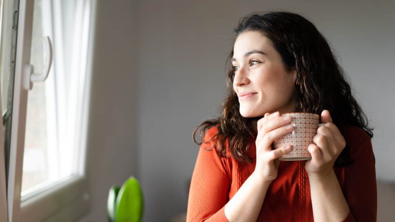 Woman drinking coffee looking out the window after reading devotions on gratitude