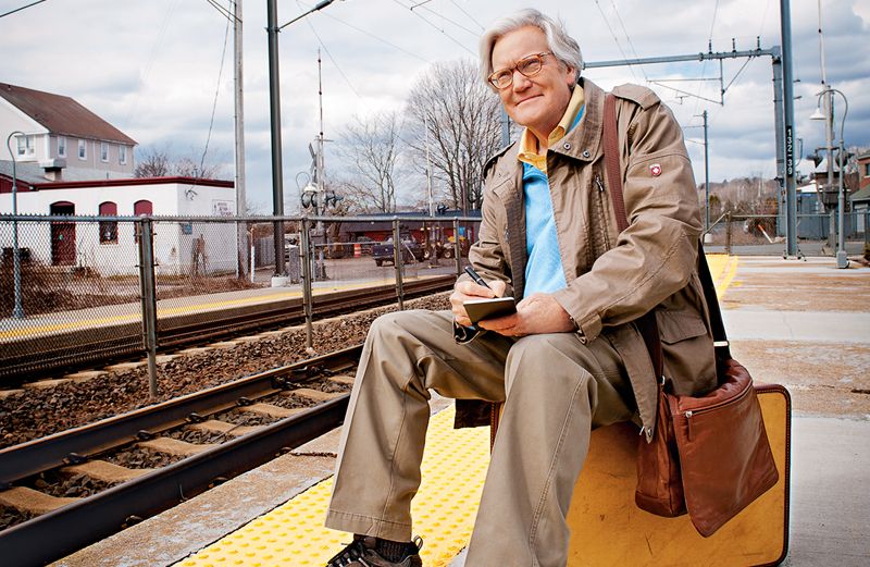 Bob Dotson sits on a suitcase on a railroad platform.