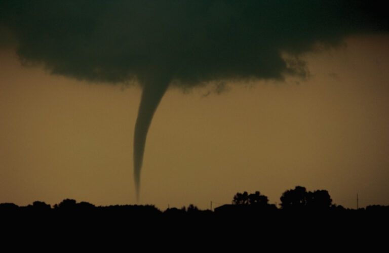 A funnel cloud dips down from dark, stormy clouds.