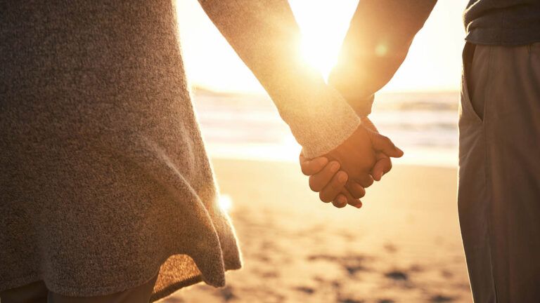 Married couple holding hands on the beach after reading marriage devotions