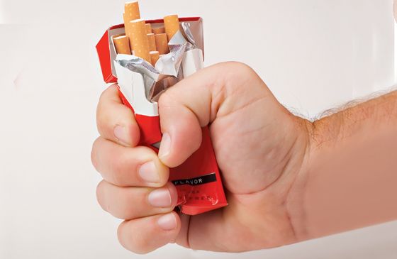 A man's hand crumples a pack of cigarettes.