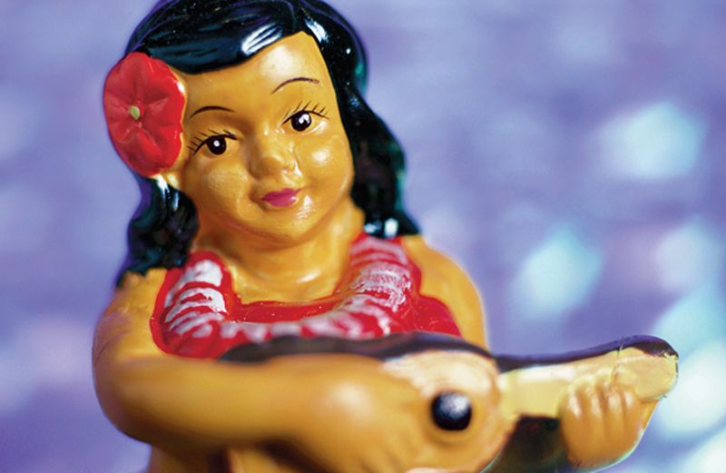A figurine of a grass-skirted hula girl, strumming a ukulele