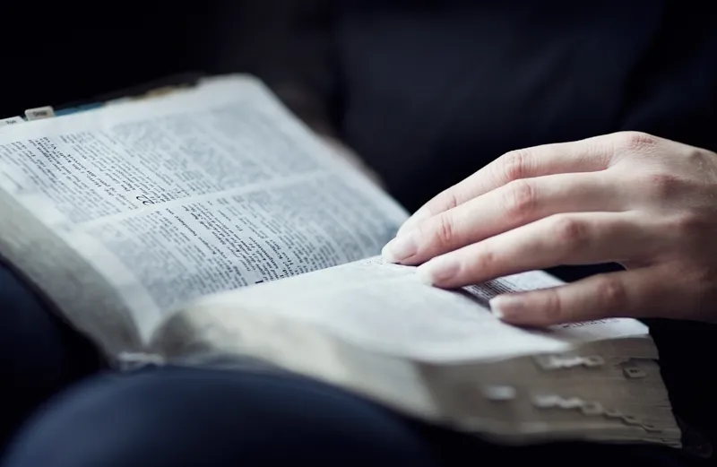 An open Bible with a woman's hand resting upon it