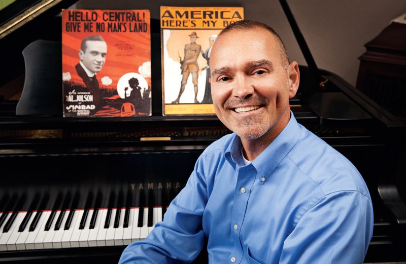 Bobby Simma sits at a piano with several copies of sheet music
