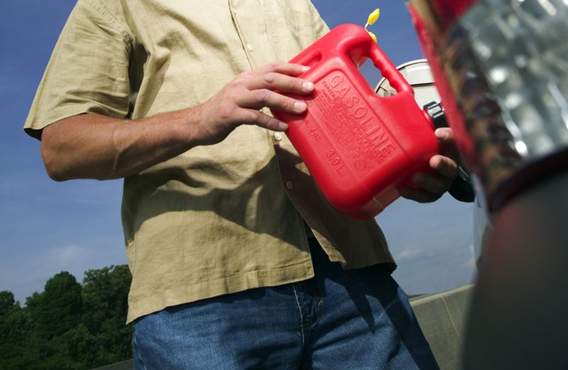 A man uses a gas can to fill a car's empty gas tank.