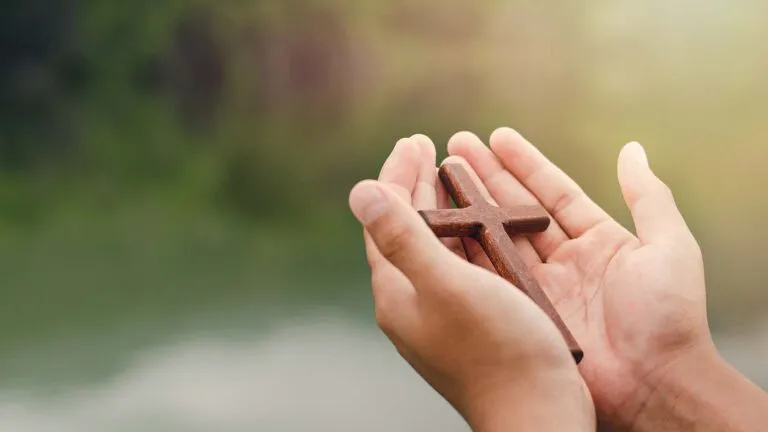 Two hands holding a wooden cross for the message of Easter