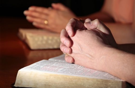close-up of a people praying together with hands on Bibles