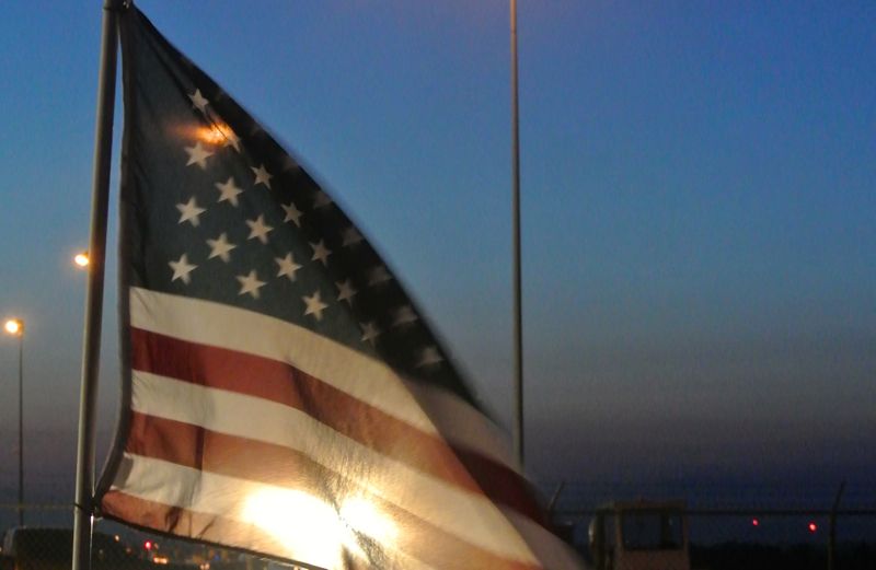 An American flag backlit by a lamppost at night