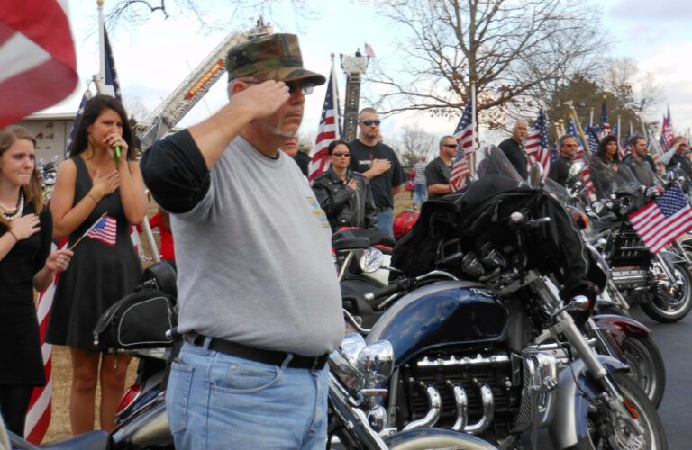 A line of Patriot Guards saluting at a fallen Army medic's funeral