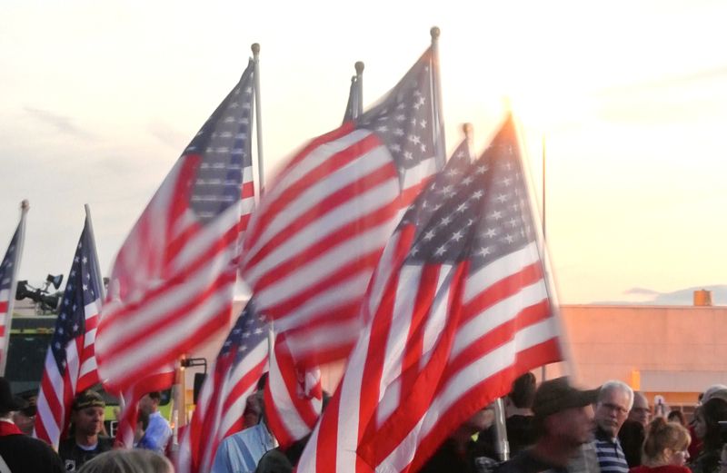 American flags waving in a crowd with sunlight behind them