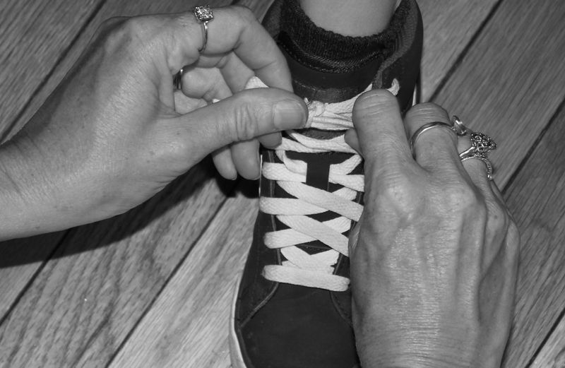 A photograph of a mother's hands tying a young boy's shoelaces.