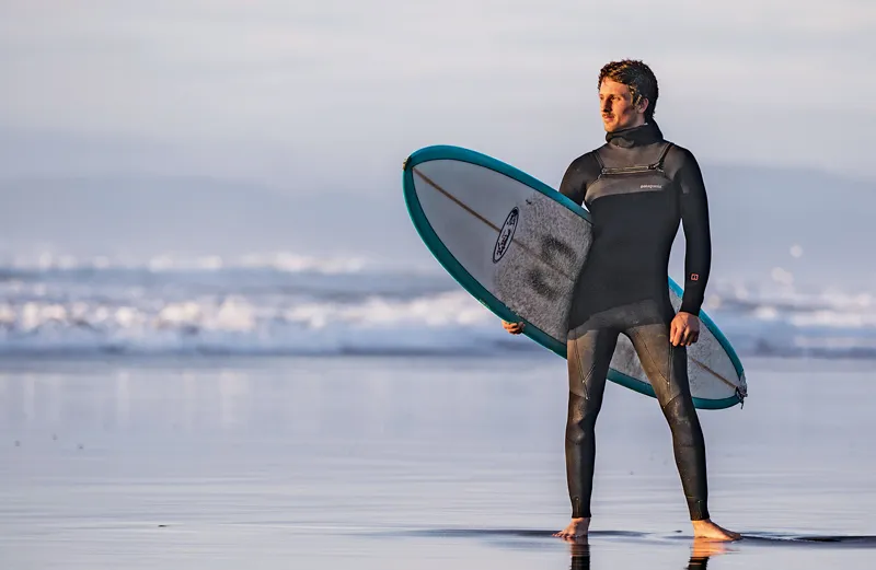 Scott Stephens stands on the beach, surfboard under his arm.