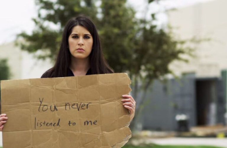 A woman holds up a handwritten sign, reading "You never listened to me."