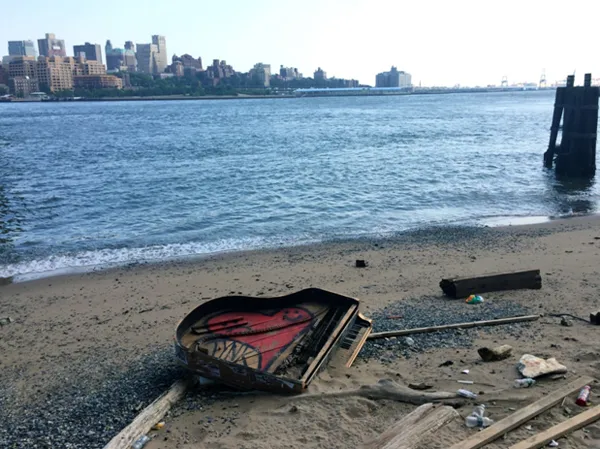 A smiling red heart painted inside the remains of a grand piano on the bank of the East River