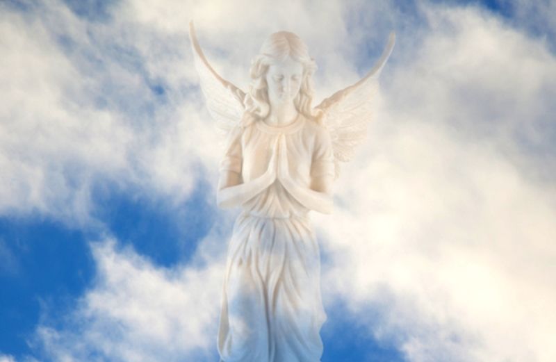 A photo composite of an angel statue against a blue sky with clouds.