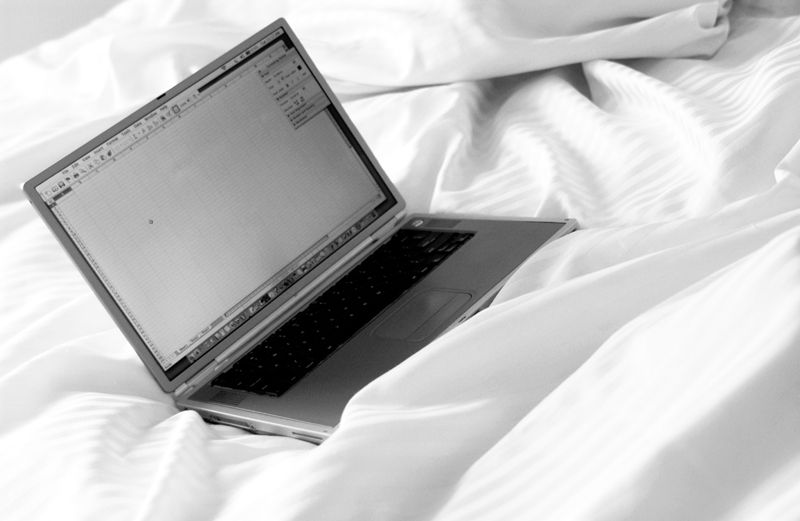 An open laptop sitting on rumpled bedsheets