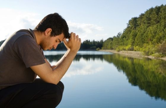 man praying in front of a lake with mountains behind him.