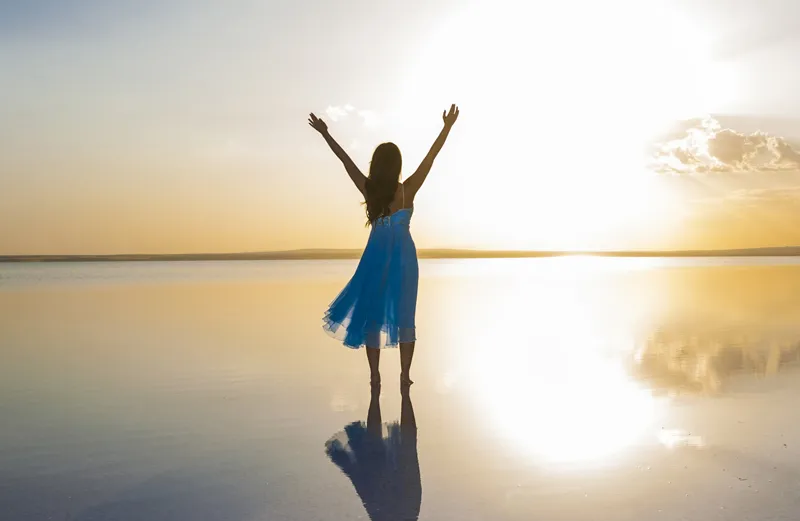 A photograph of a woman lifting her hands while standing on the beach