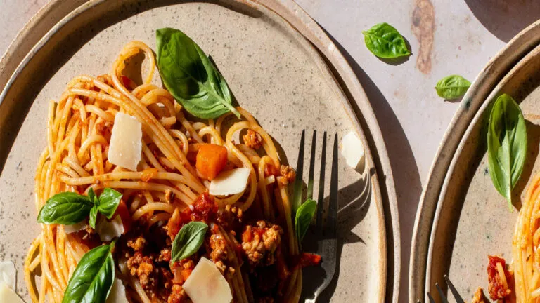 Two plates of spaghetti with basil and parmesan cheese.