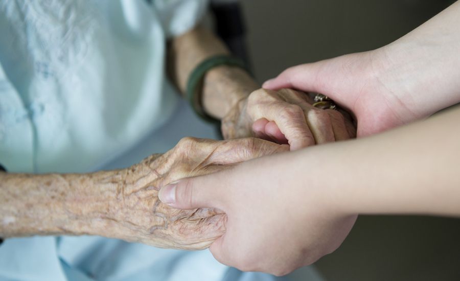 An elderly woman's hands are clasped lovingly by a younger woman's hands.