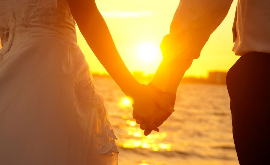 Newlyweds hold hands on a sun-splashed beach.