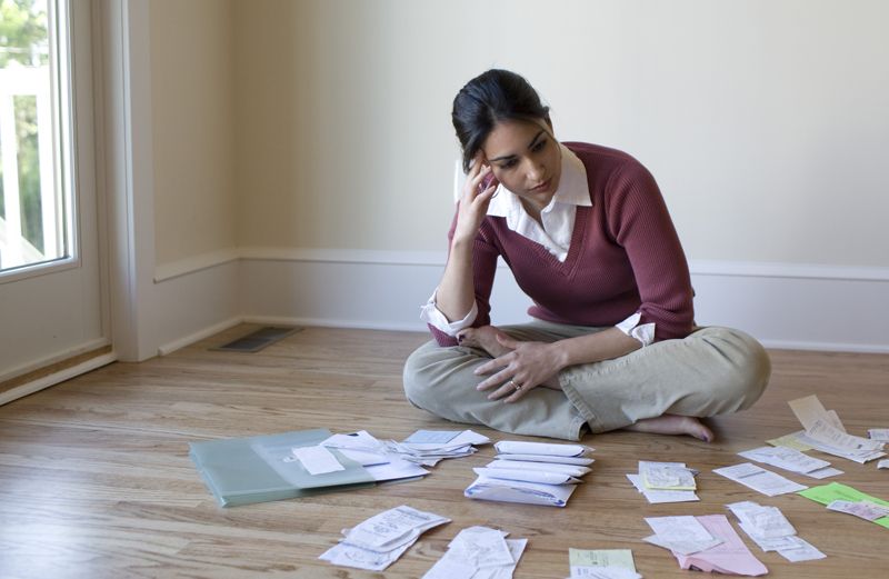 A woman sits on the floor, worried, while surrounded by unpaid bills.