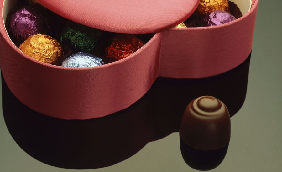 A single chocolate alongside a big heart-shaped box of candy