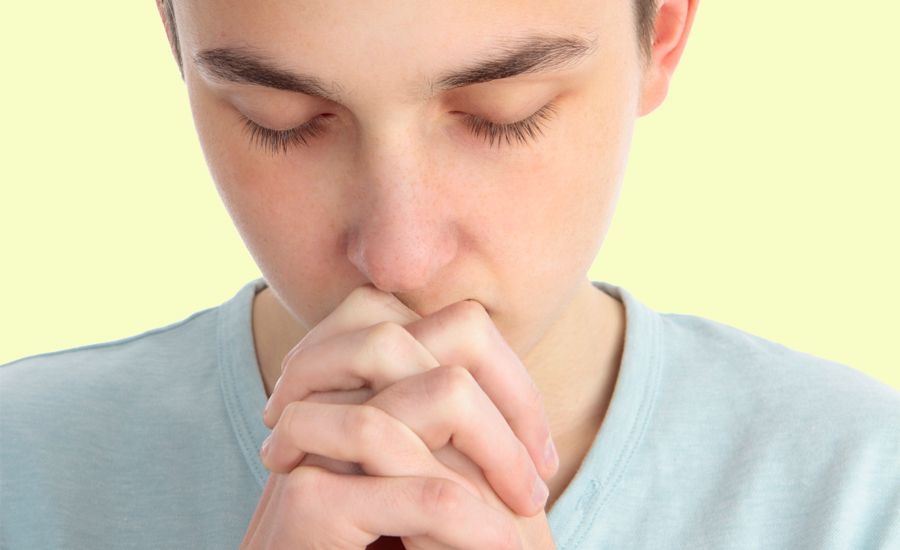 A teenage boy clasps his hands in prayer.
